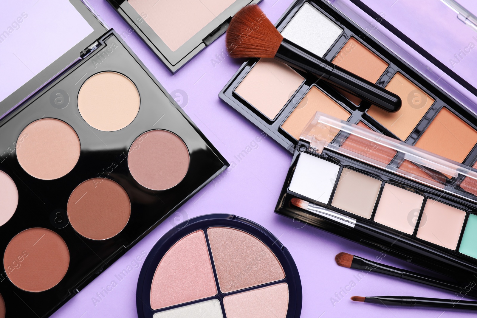 Photo of Colorful contouring palettes with brushes on violet background, flat lay. Professional cosmetic product