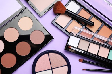 Photo of Colorful contouring palettes with brushes on violet background, flat lay. Professional cosmetic product