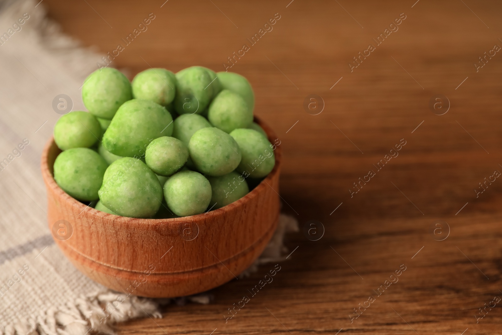 Photo of Tasty wasabi coated peanuts in bowl on brown wooden table, closeup. Space for text