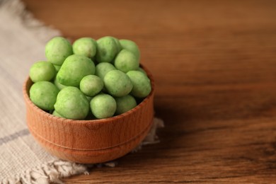 Photo of Tasty wasabi coated peanuts in bowl on brown wooden table, closeup. Space for text