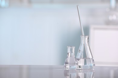 Laboratory analysis. Glass flasks and stirring rod on white table against blurred background, space for text