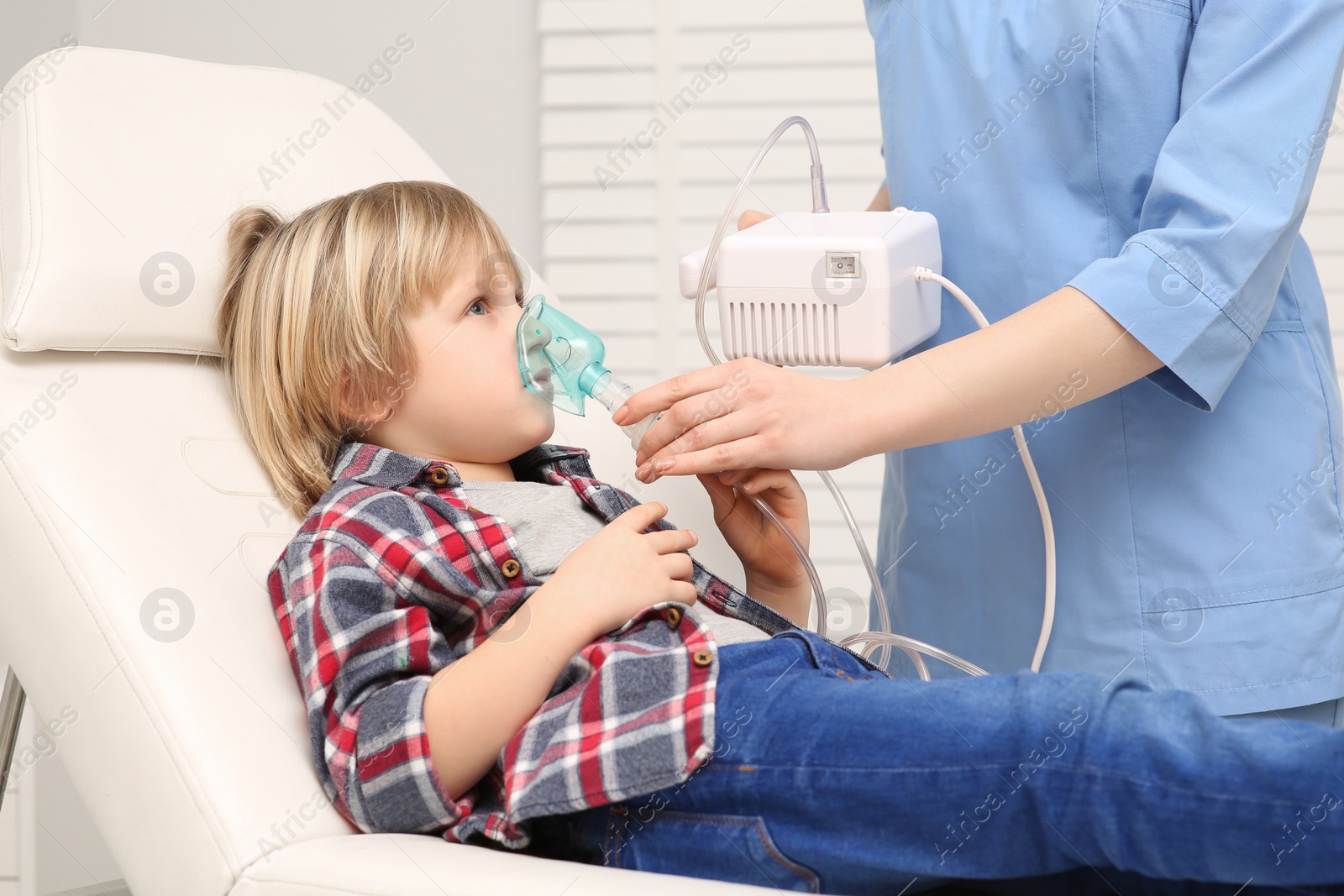 Photo of Medical assistant helping sick little boy with nebulizer inhalation at hospital