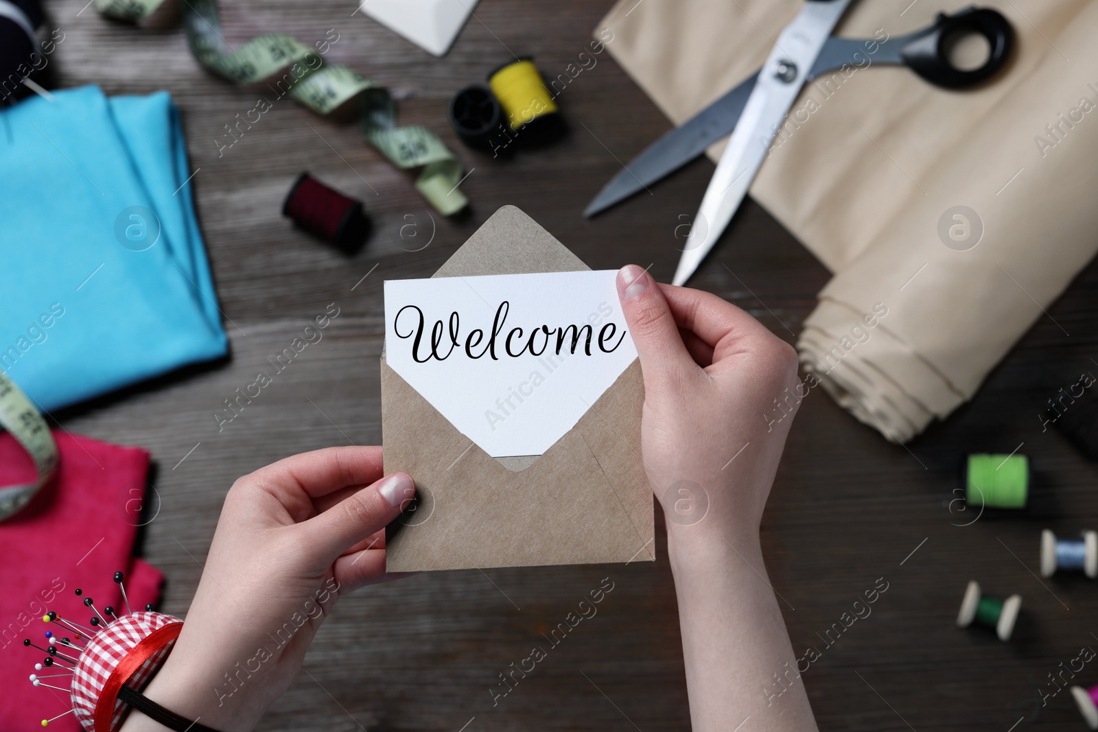 Image of Seamstress taking paper note with word Welcome out of envelope at table in atelier, closeup