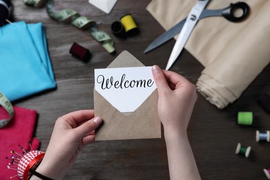 Image of Seamstress taking paper note with word Welcome out of envelope at table in atelier, closeup