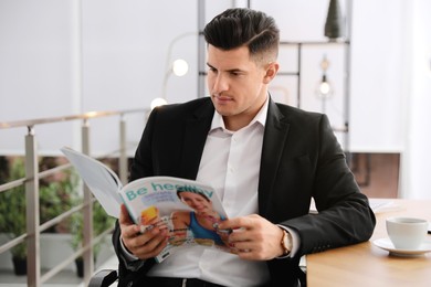 Photo of Man reading magazine at table in office