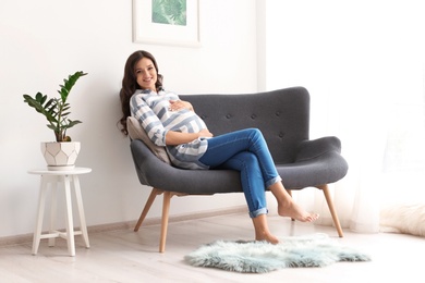 Beautiful pregnant woman sitting on sofa at home