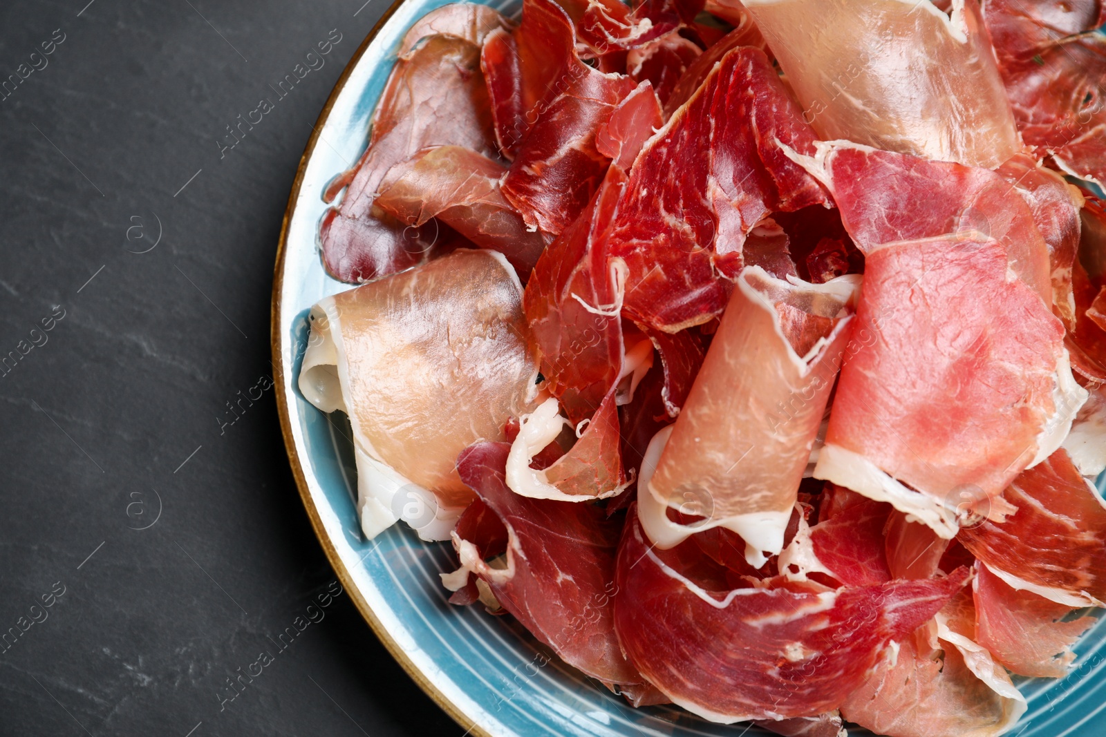 Photo of Tasty fresh prosciutto on black table, top view