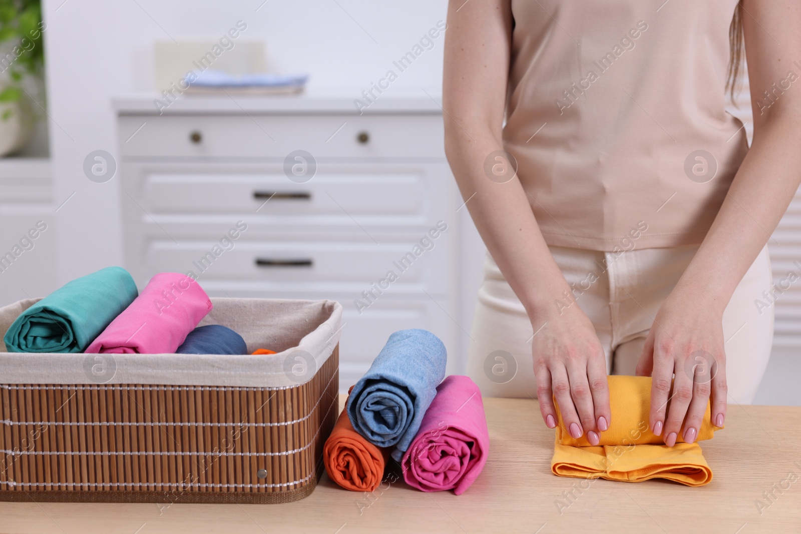 Photo of Woman rolling shirt at table in room, closeup. Organizing clothes