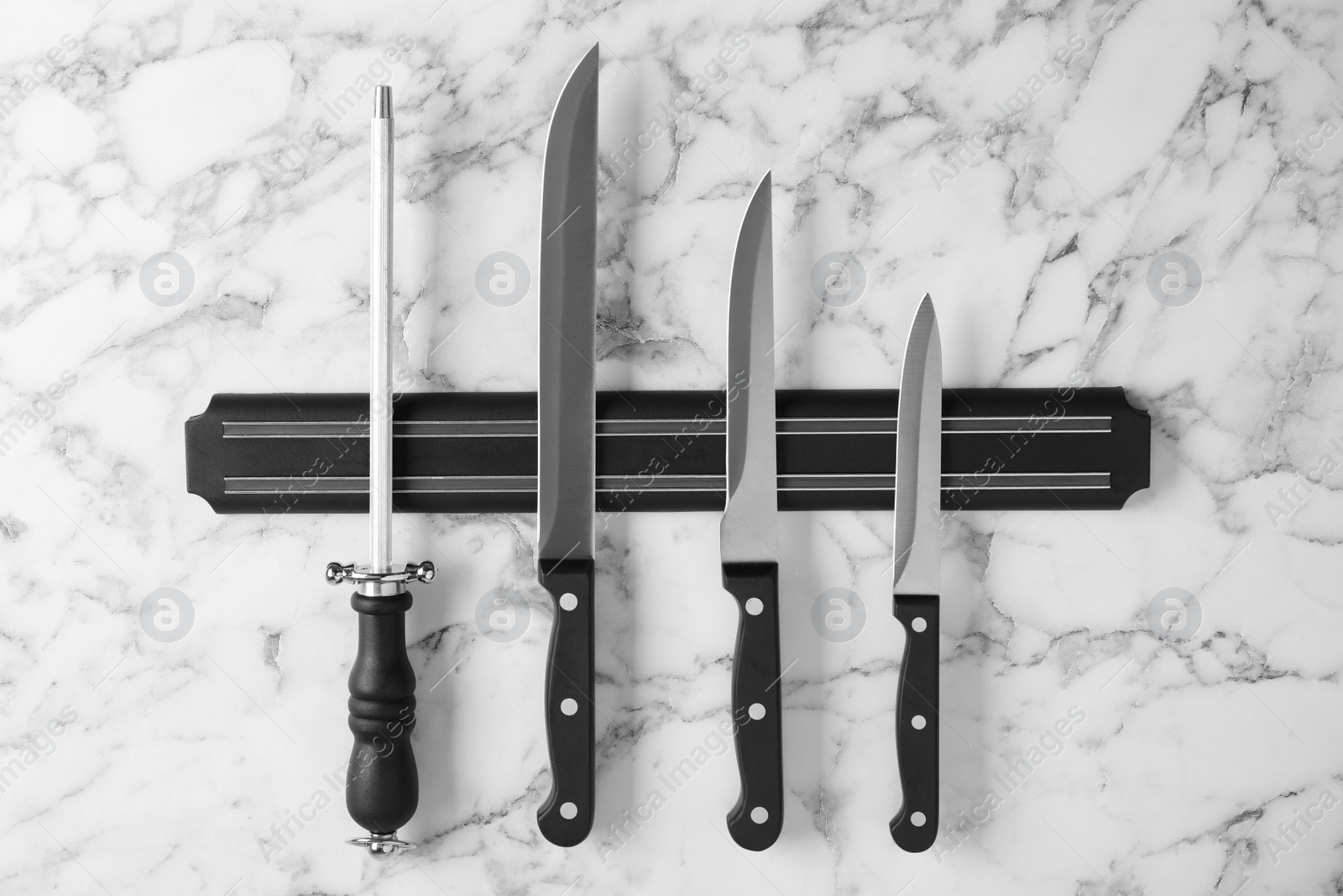 Photo of Magnetic holder with set of knives and sharpener on marble background