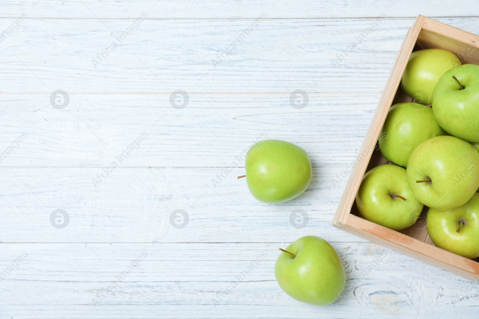 Photo of Wooden crate full of fresh green apples on light background, top view. Space for text