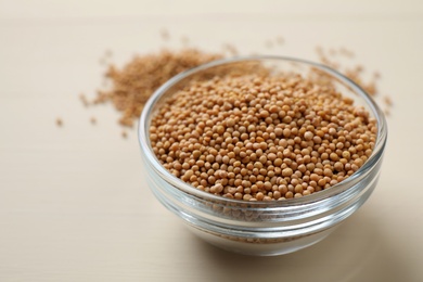 Photo of Mustard seeds in glass bowl on white wooden table, closeup