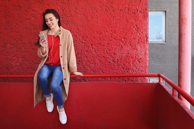 Photo of Young woman using phone for listening to music outdoors