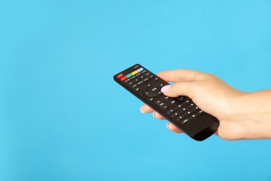 Woman holding remote control on light blue background, closeup. Space for text