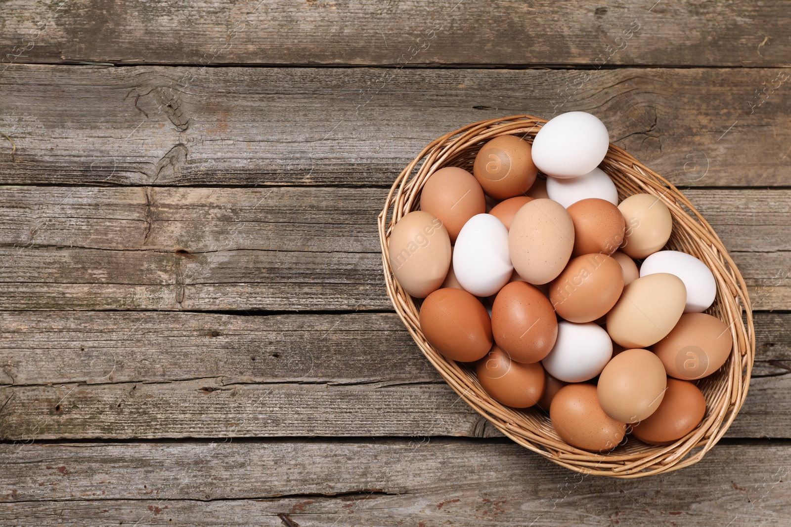 Photo of Fresh chicken eggs in wicker basket on wooden table, top view. Space for text