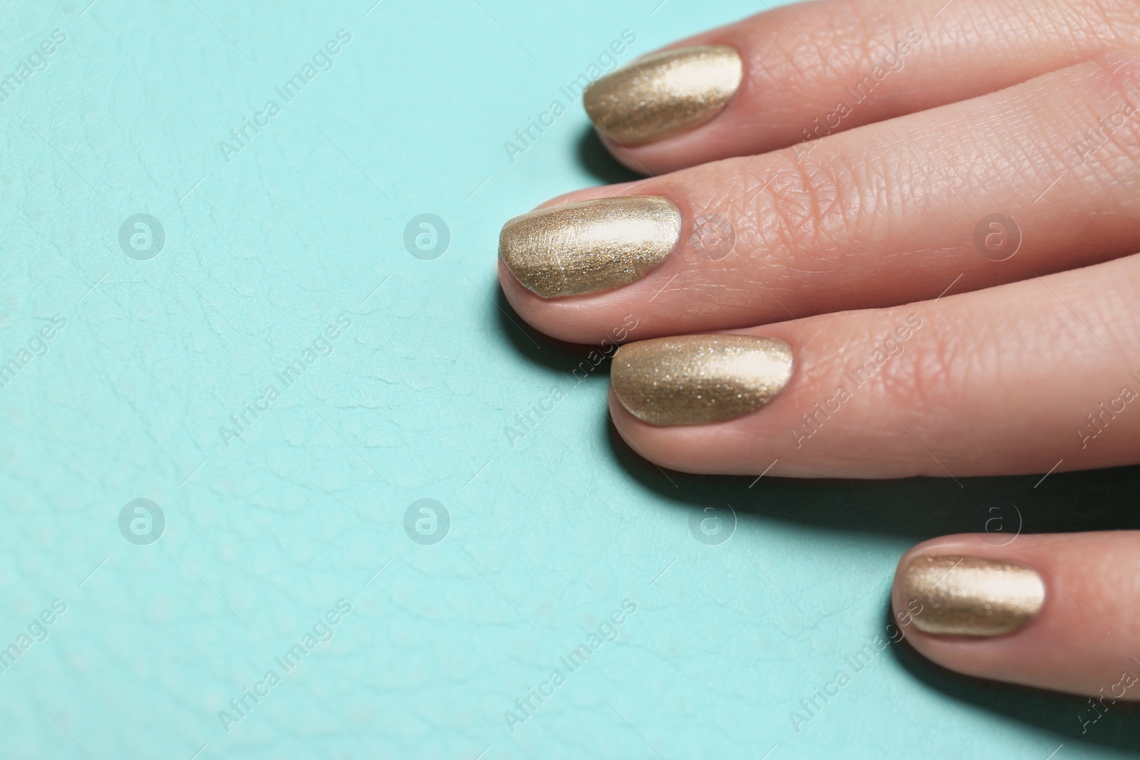 Photo of Woman showing golden manicure on color background, closeup with space for text. Nail polish trends