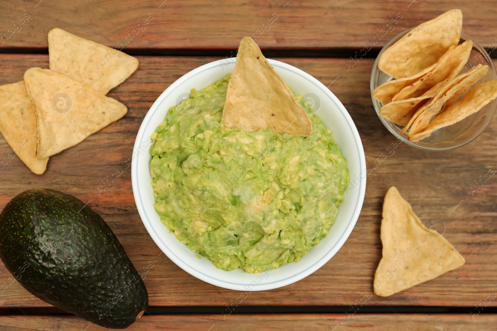 Photo of Delicious guacamole, avocado and nachos on wooden table, flat lay