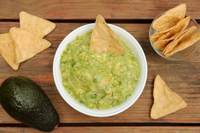 Delicious guacamole, avocado and nachos on wooden table, flat lay