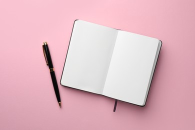 Photo of Open notebook with blank pages and pen on light pink background, top view. Space for text