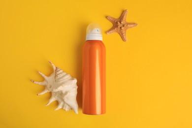 Bottle of sunscreen, starfish and seashell on yellow background, flat lay