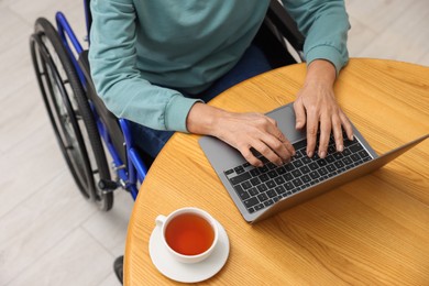 Woman in wheelchair using laptop at wooden table, above view
