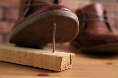 Metal nail in wooden plank and shoes on table, closeup