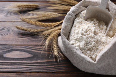 Photo of Sack with flour and wheat spikes on wooden background, above view