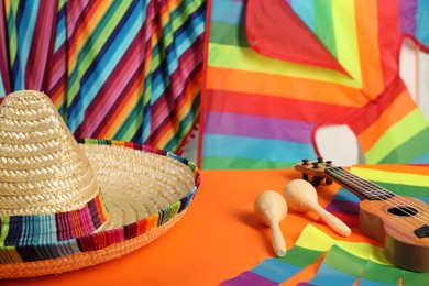 Mexican sombrero hat, ukulele and maracas on orange table, closeup