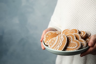 Photo of Woman holding plate with tasty heart shaped gingerbread cookies on blue background, closeup. Space for text