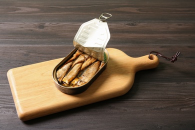 Photo of Board with tin can of sprats on wooden table