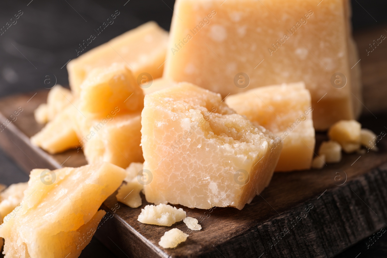 Photo of Pieces of delicious parmesan cheese on wooden board, closeup