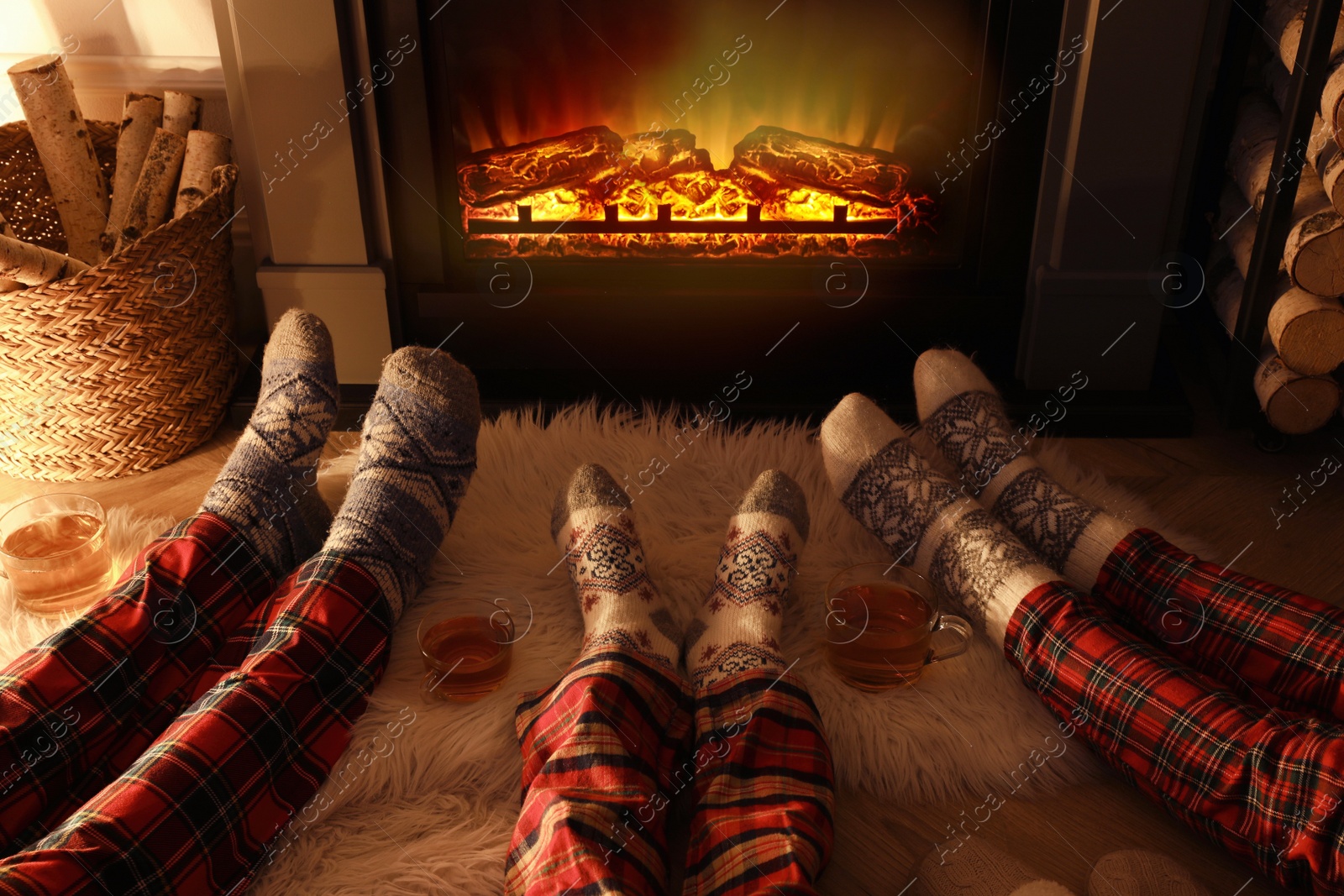 Photo of Family in warm socks resting near fireplace at home, closeup of legs