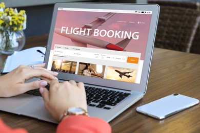 Woman using laptop to book flight at wooden table, closeup