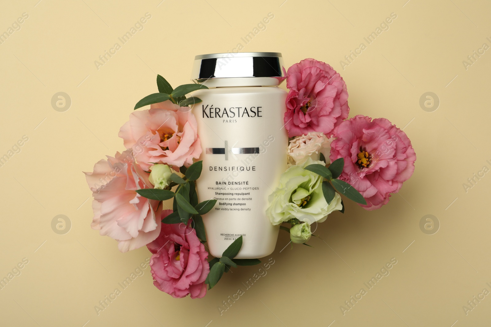 Photo of MYKOLAIV, UKRAINE - SEPTEMBER 07, 2021: Kerastase shampoo and beautiful flowers on beige background, flat lay. Hair care cosmetic product