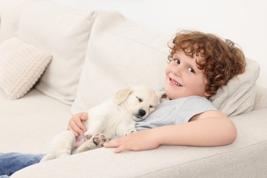 Photo of Little boy hugging cute puppy on couch