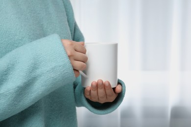 Photo of Woman holding white mug indoors, closeup. Mockup for design