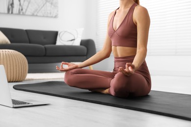 Woman practicing Padmasana with laptop on yoga mat at home, closeup. Lotus pose