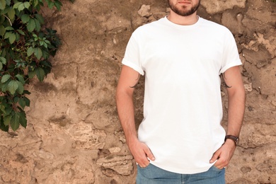 Young man wearing white t-shirt near stone wall on street