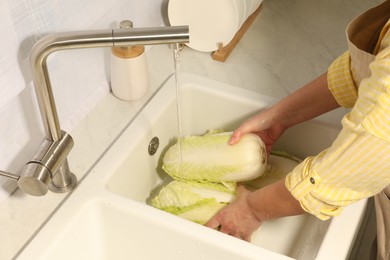 Photo of Woman washing fresh chinese cabbage under tap water in kitchen sink, closeup