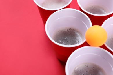 Plastic cups and ball on red background, space for text. Beer pong game