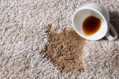 Photo of Overturned cup and spilled coffee on beige carpet, closeup