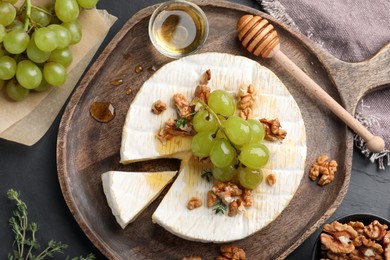 Photo of Brie cheese served with grapes, walnuts and honey on grey table, flat lay