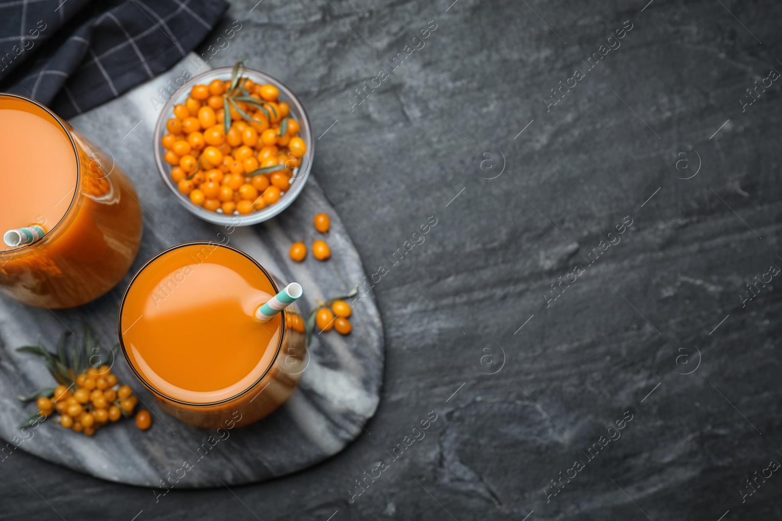 Photo of Delicious sea buckthorn juice and fresh berries on black table, top view. Space for text