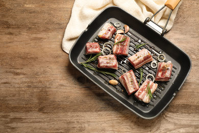 Photo of Grill pan with raw ribs and seasonings on wooden table, top view. Space for text
