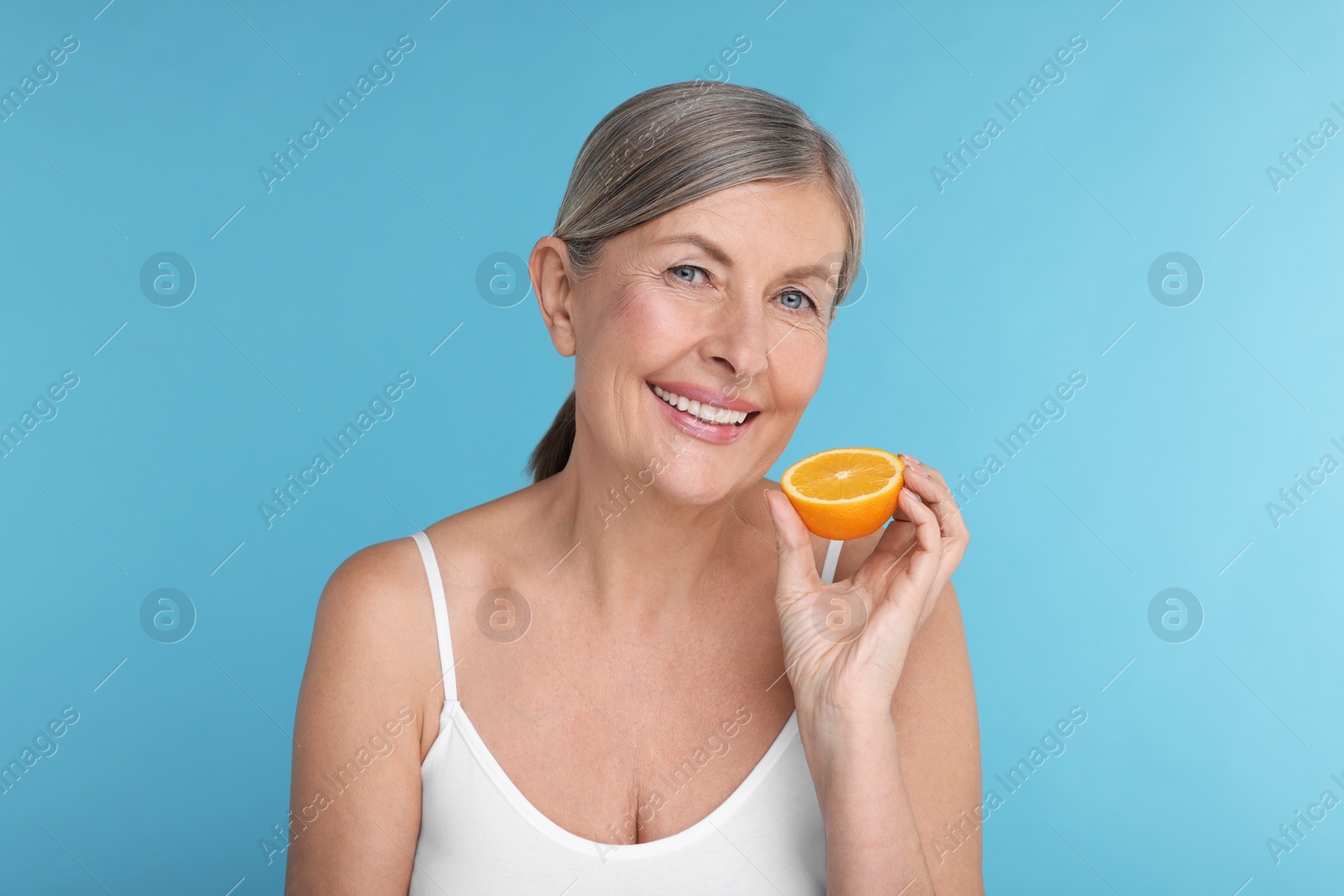 Photo of Beautiful woman with half of orange rich in vitamin C on light blue background