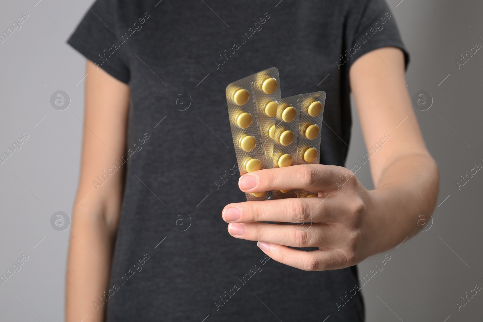 Photo of Woman holding pills in blister packs on gray background, closeup