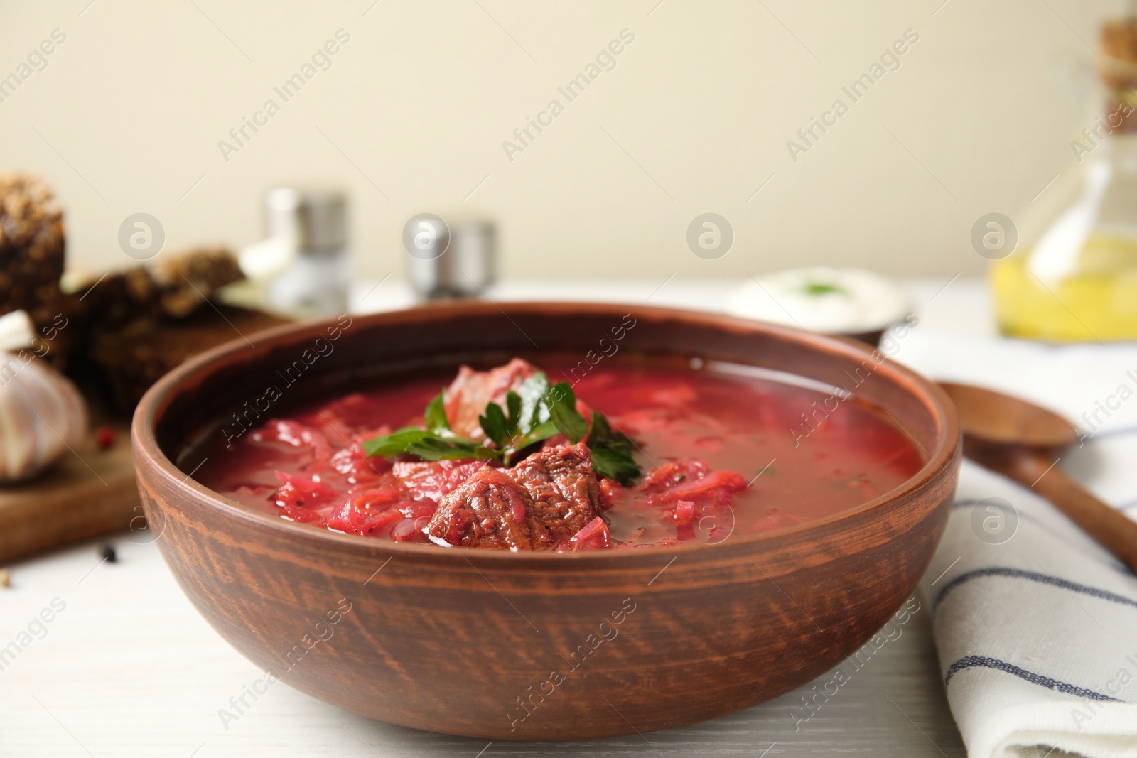 Photo of Stylish brown clay bowl with Ukrainian borsch served on white wooden table