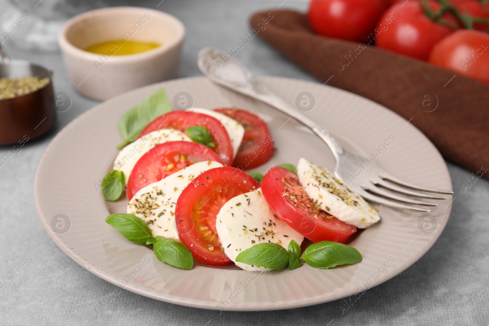 Photo of Delicious Caprese salad with tomatoes, mozzarella, basil and spices on light grey table, closeup