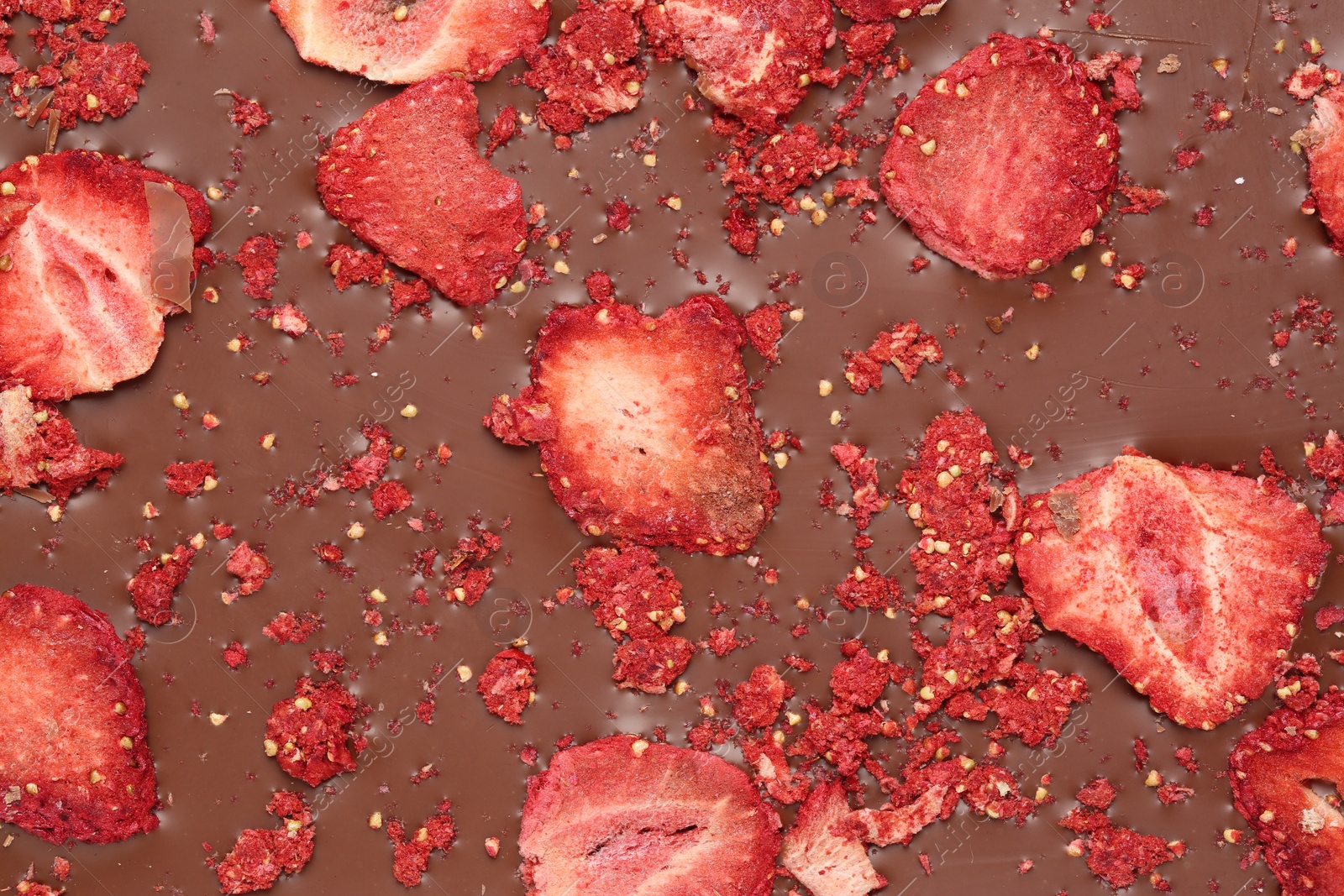 Photo of Chocolate bar with freeze dried strawberries as background, closeup