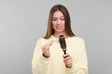 Photo of Emotional woman untangling her lost hair from brush on light grey background. Alopecia problem