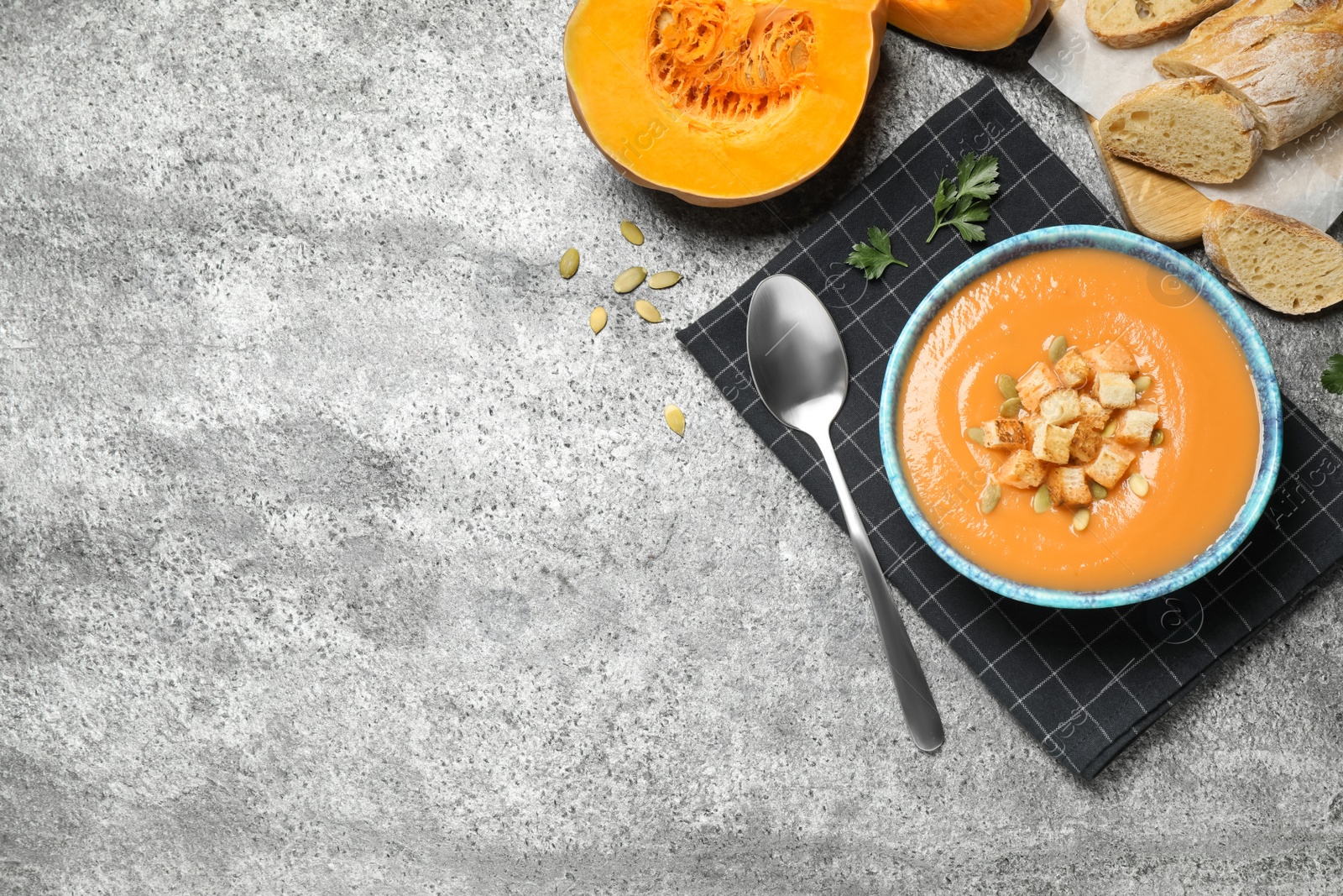 Photo of Tasty creamy pumpkin soup served with bread on grey table, flat lay. Space for text